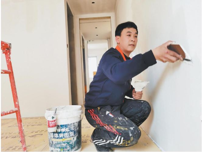 白保林在给墙面刮腻子（资料照片）
